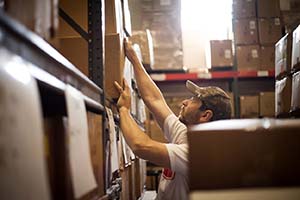 Warehouse jobs are physical. Worker reaching up for a package stored in the warehouse.